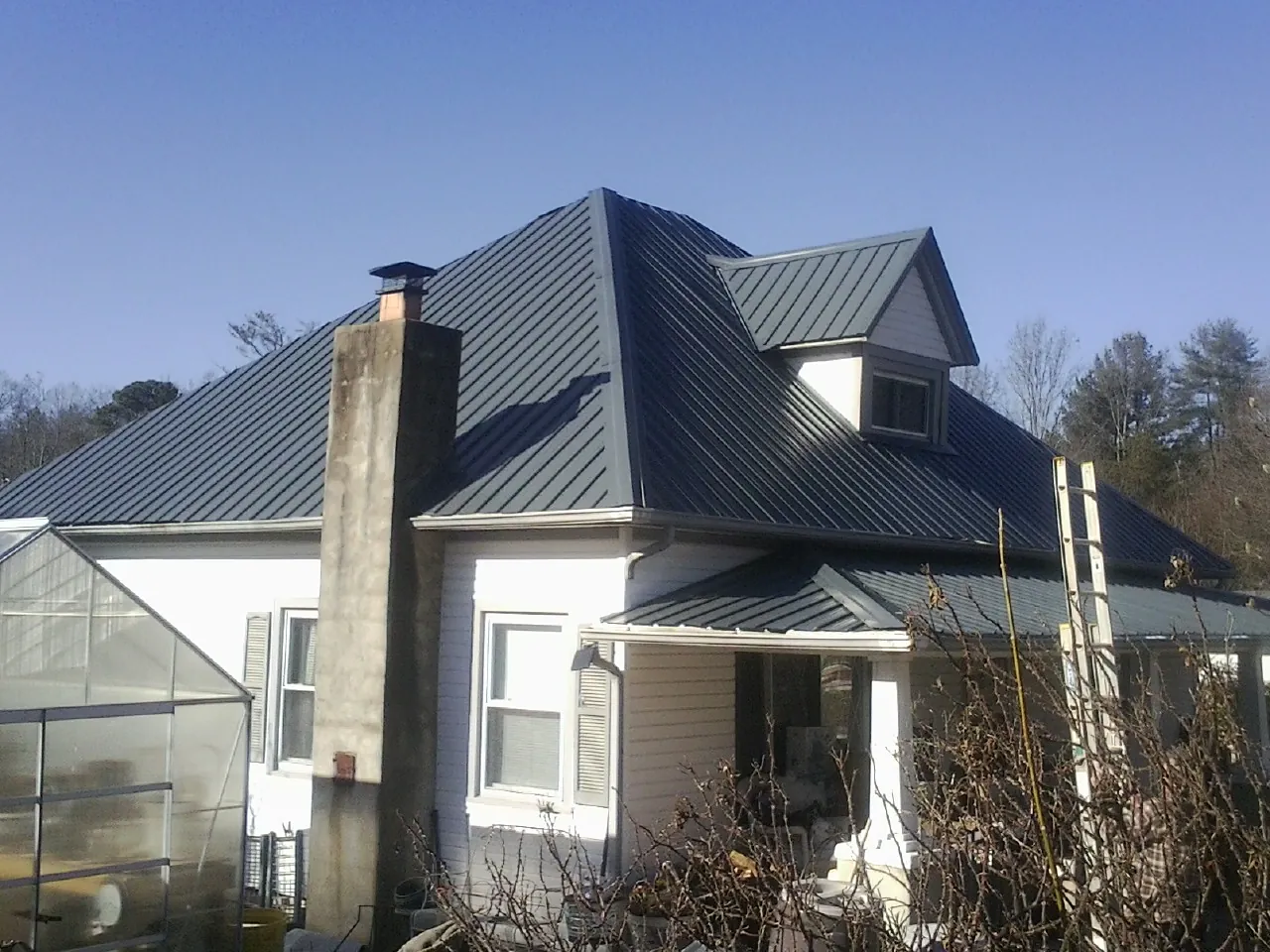 Dark blue standing seam metal roof on a white farmhouse with dormer — Slate & Tile Roof Repair by Roofing Brothers in Osco