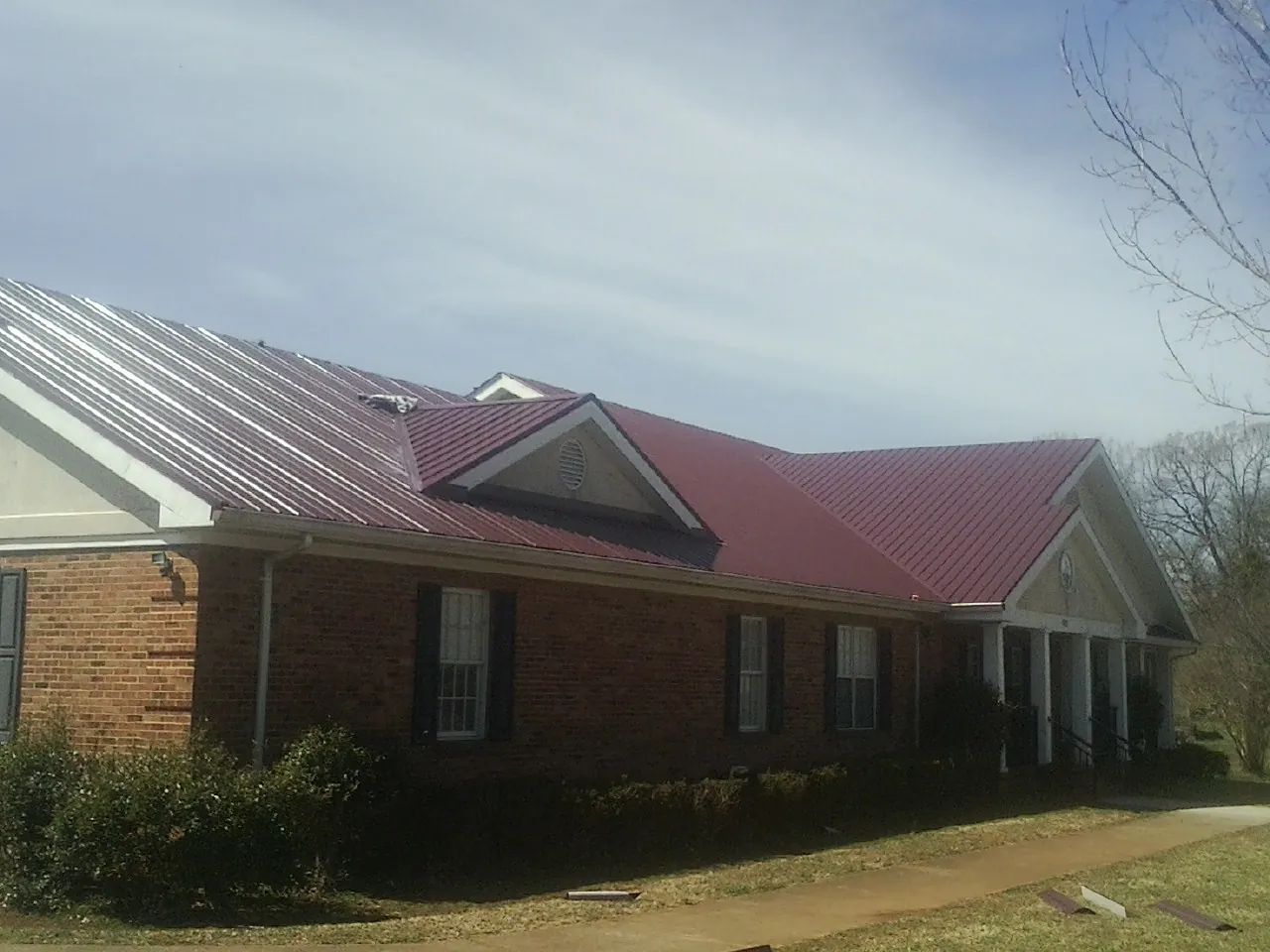 Red metal roof with gabled entries on a long brick building, from a Hail Damage Roof Repair job in Osco