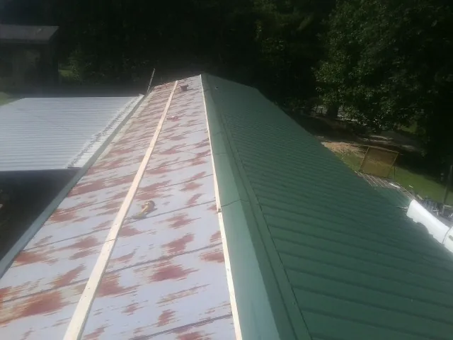 Old rusted panels beside newly installed green metal roofing — Wind Damage Roof Repair by Roofing Brothers in Osco