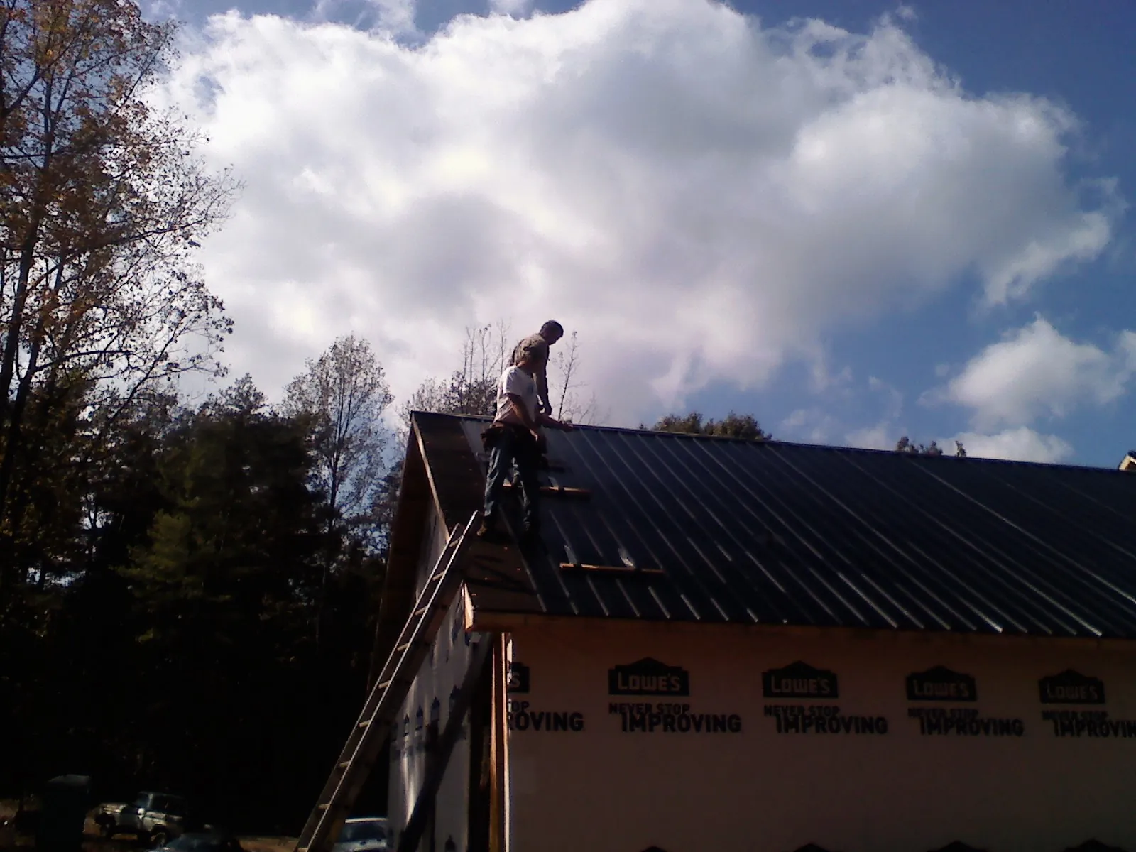 Roofer fastening dark metal panels high against a cloudy sky, from a Roof Inspection job in Osco